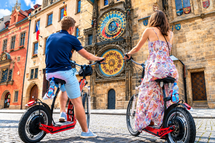Two people on scooters facing a large historic clock on a building.