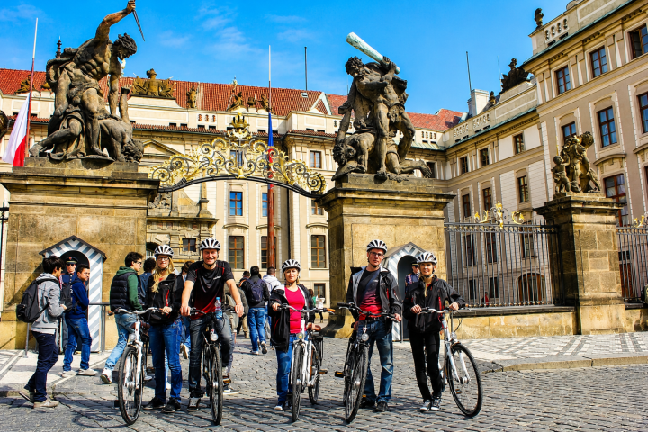 Group of cyclists pose in front of ornate gate at historic building.
