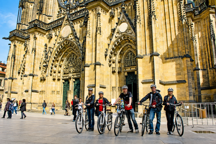 Group of cyclists in front of a historic building with arched entrances.