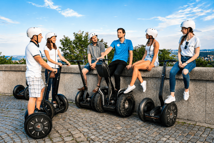 Group of six people with helmets on Segways, having a conversation outdoors.
