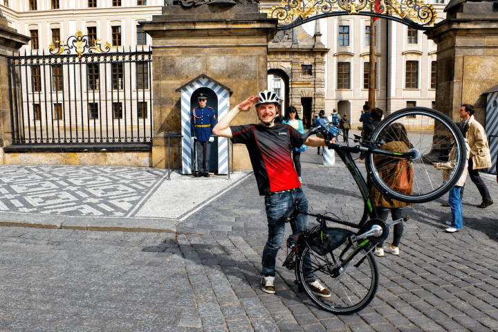 Man posing with bicycle near guarded historic building gate.