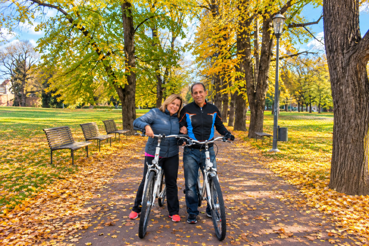 Couple with bikes on a leaf-covered park path in autumn.