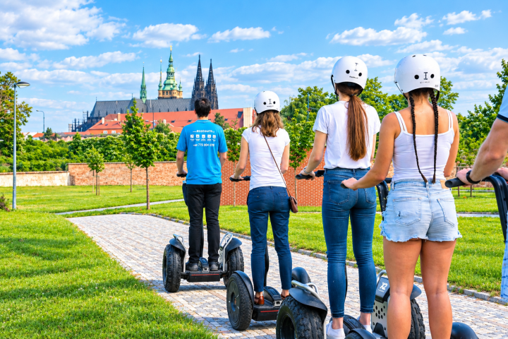 People riding Segways on a path in a park with a historic building in the background.