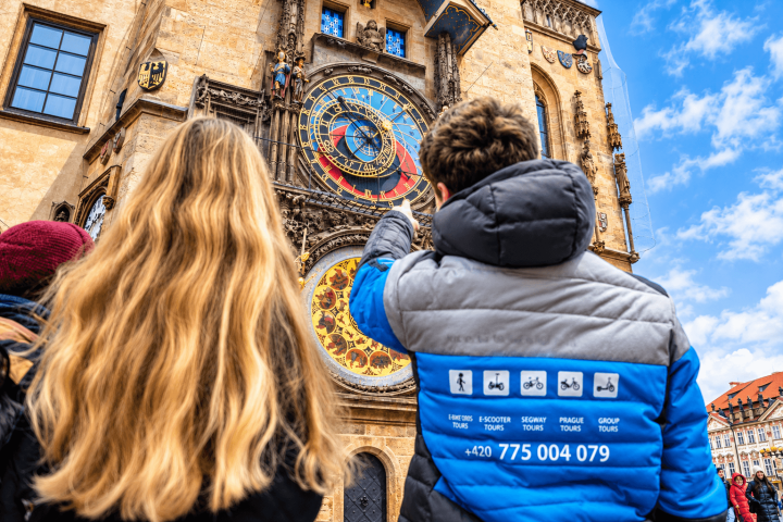 Two people view a historic astronomical clock on a building.