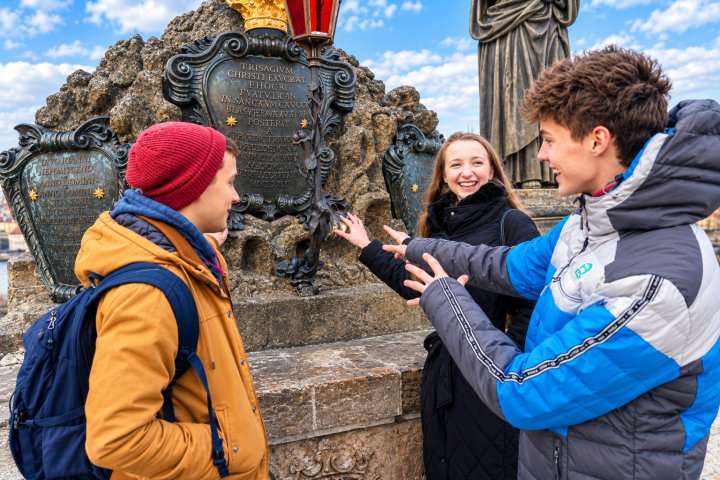 Three people smiling and talking in front of a historical plaque outdoors.