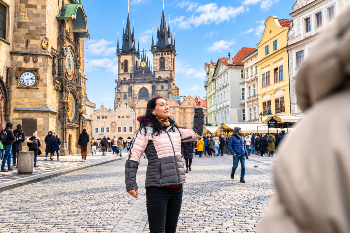 Woman posing in historic city square with clock and gothic church in background.