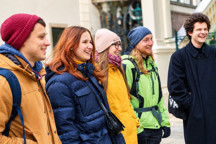 Group of five young adults in winter clothing smiling outdoors.