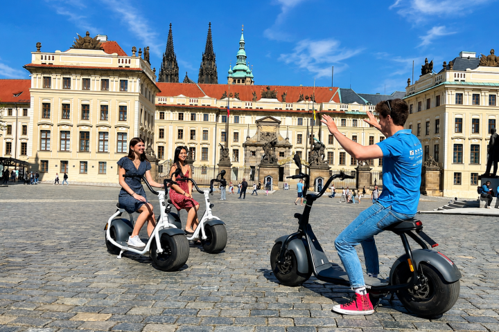 Three people on scooters in front of a historic building with ornate architecture.