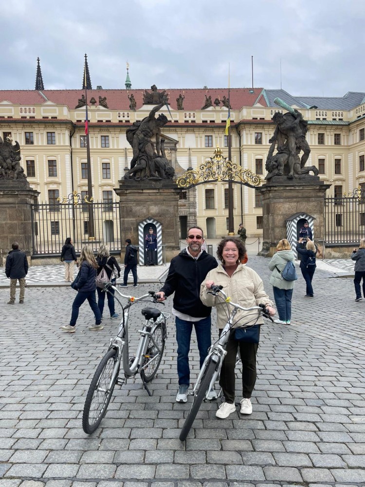 Two people with bikes in front of a historic building with statues and an ornate gate.