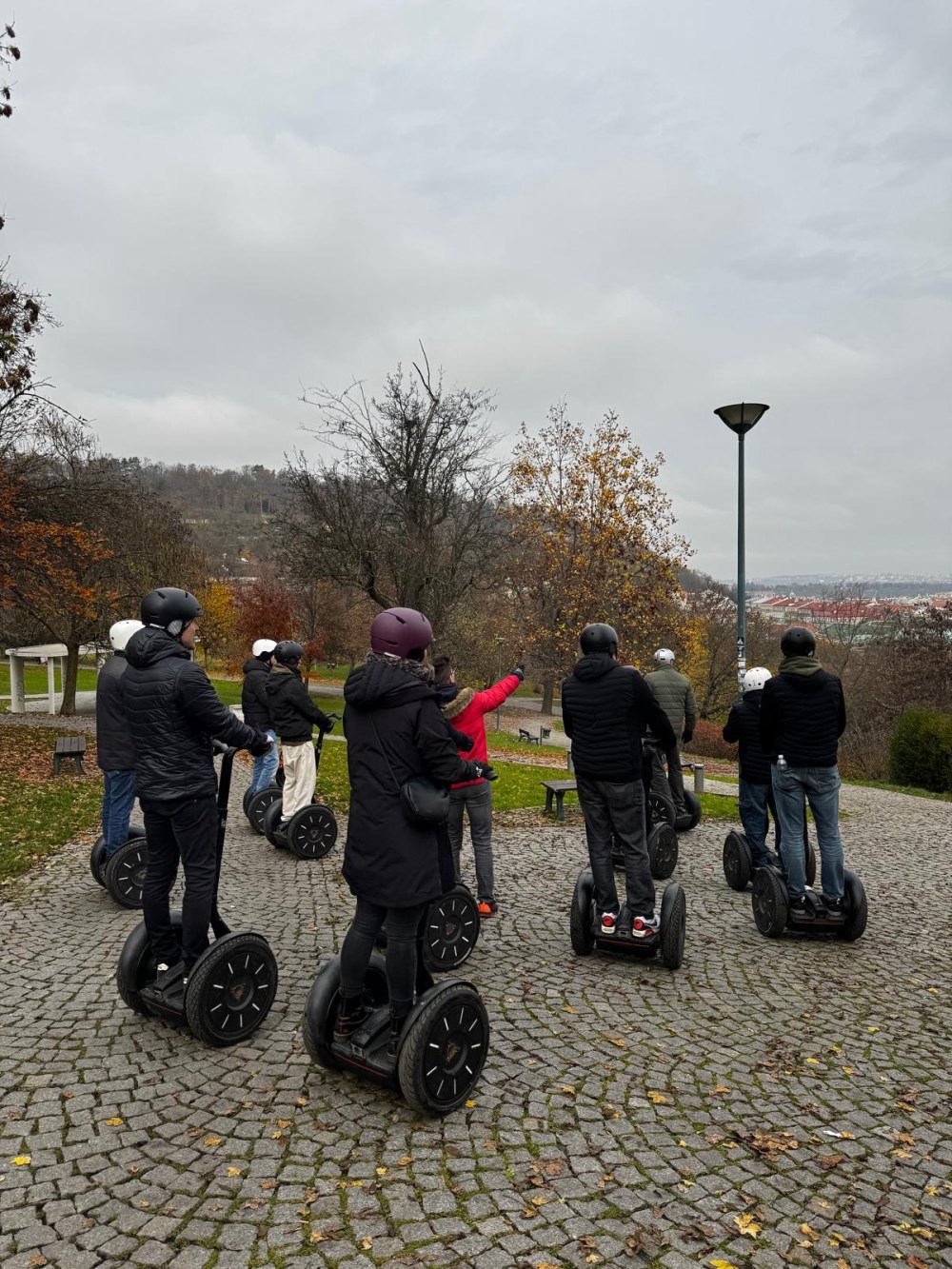 Group of people riding segways on a cobblestone path in a park during autumn.