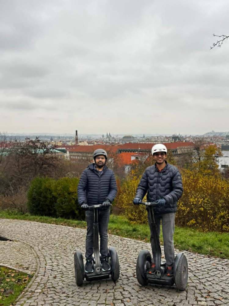 Two people on Segways on a cobblestone path with a city view in the background.