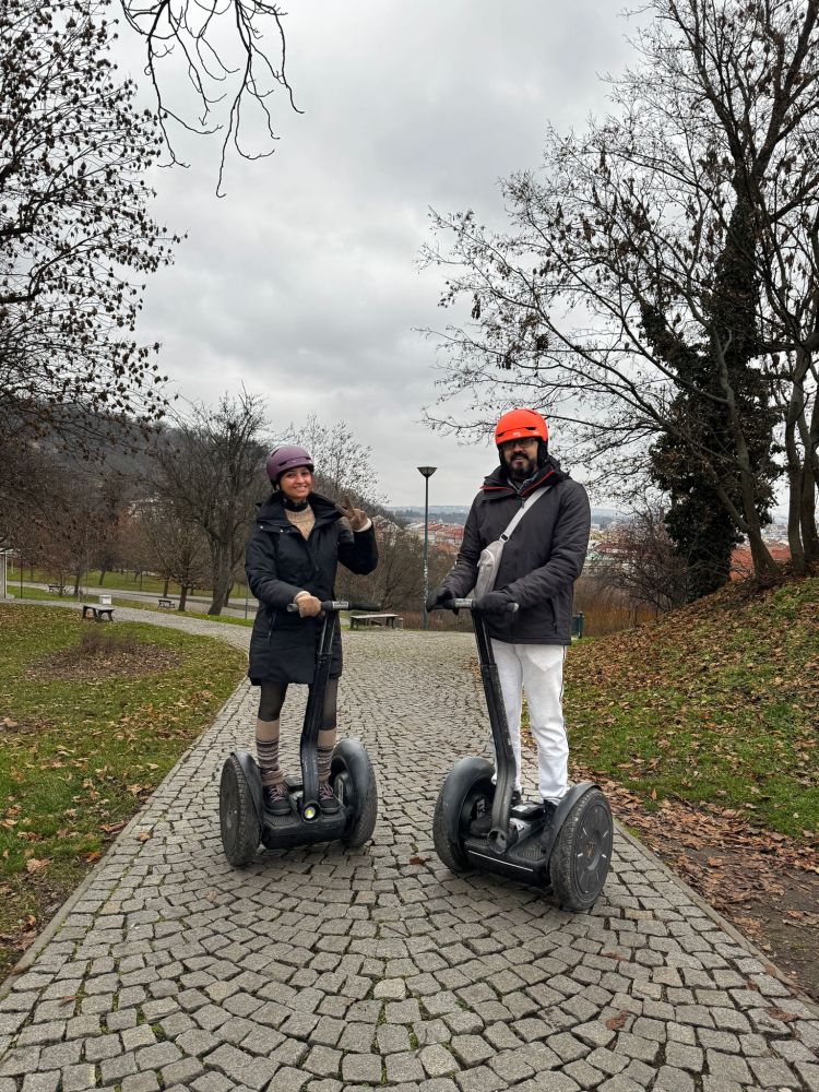 Two people on Segways in a park with bare trees and a cloudy sky.