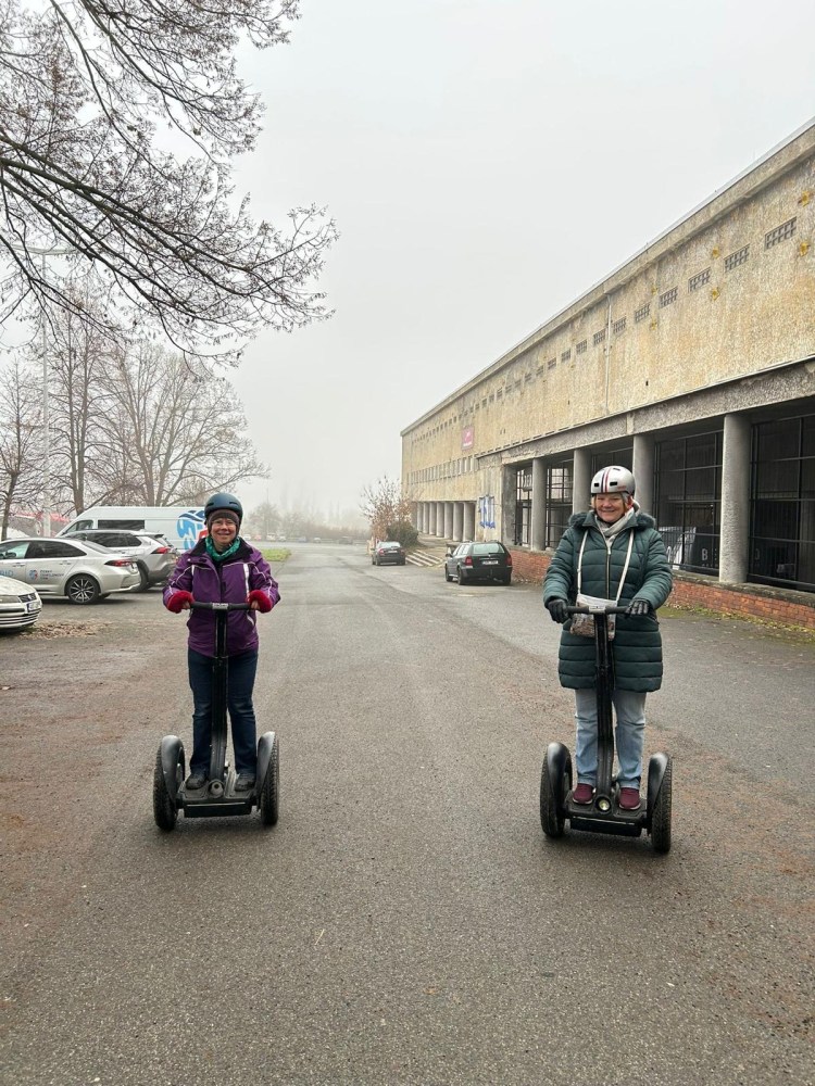 Two people riding Segways on a foggy street beside a large building.