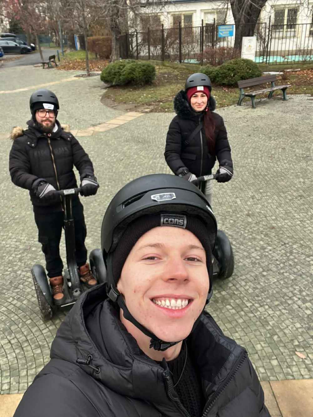 Three people with helmets riding Segways in a park, one taking a selfie.