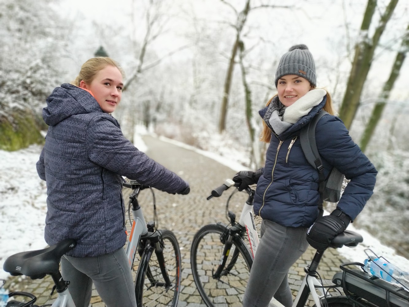 Two people in winter clothing with bikes on a snowy path.