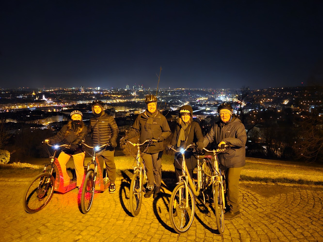 Group of five people with bicycles at night overlooking a city skyline.