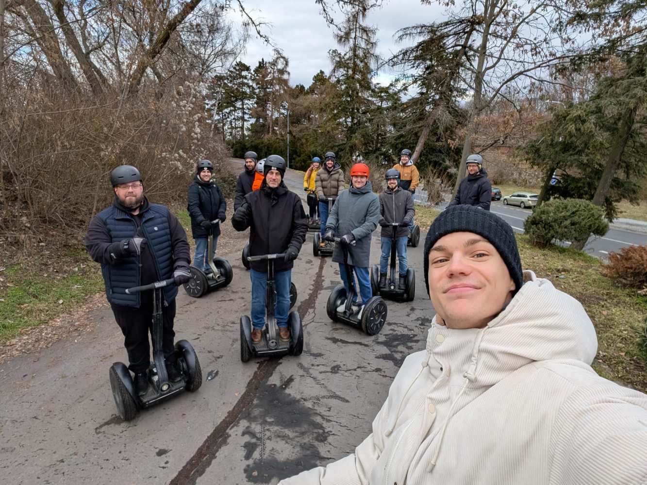 Group of people on Segways in a park, wearing helmets and winter clothes, taking a selfie.
