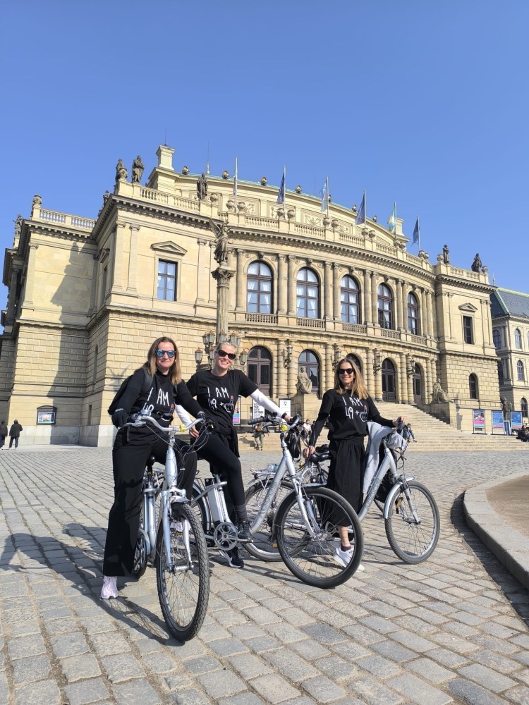 Three people on bikes in front of a historic building with blue sky background.