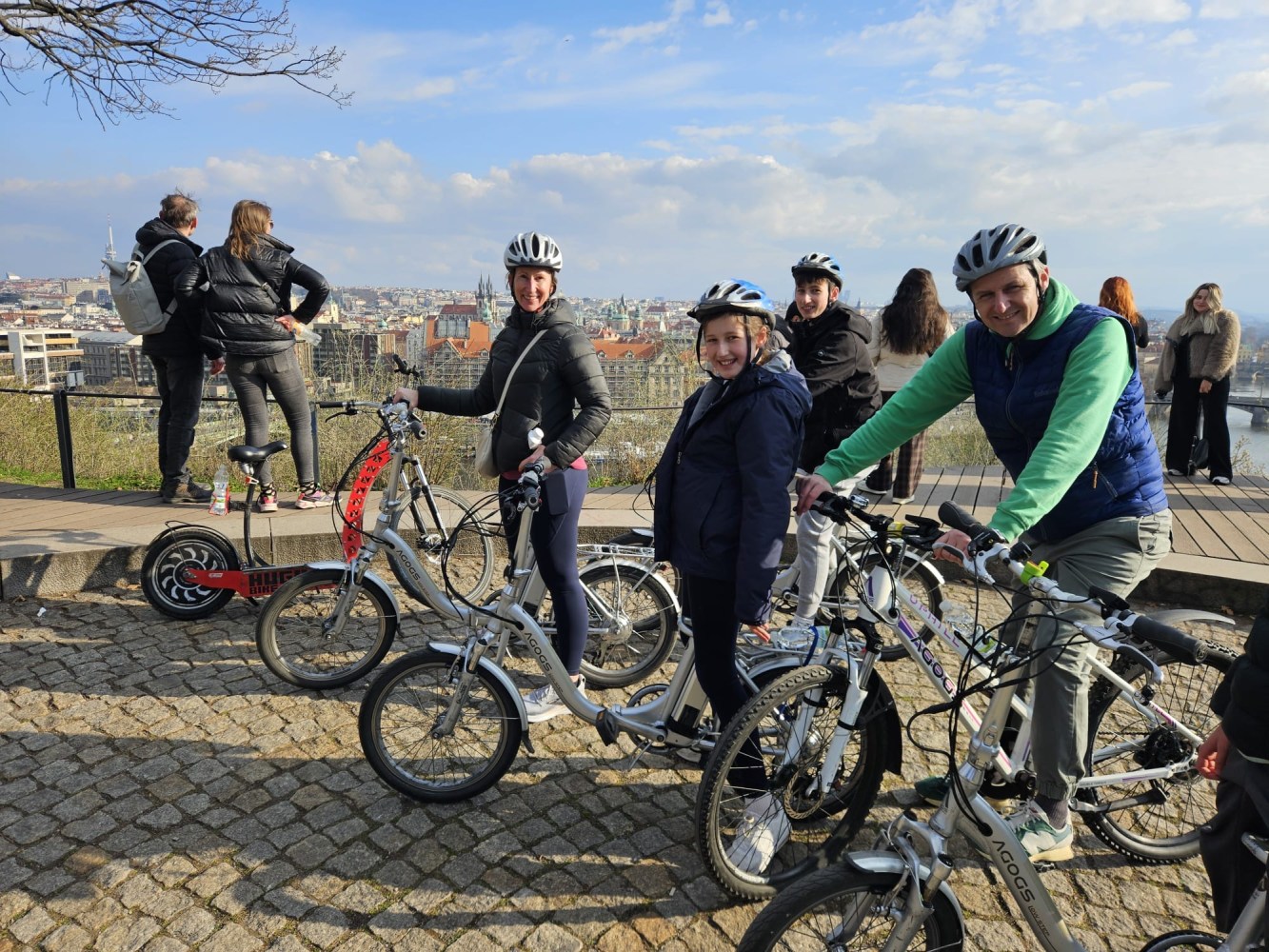 Group of people with bikes and helmets overlook a cityscape from a high vantage point.