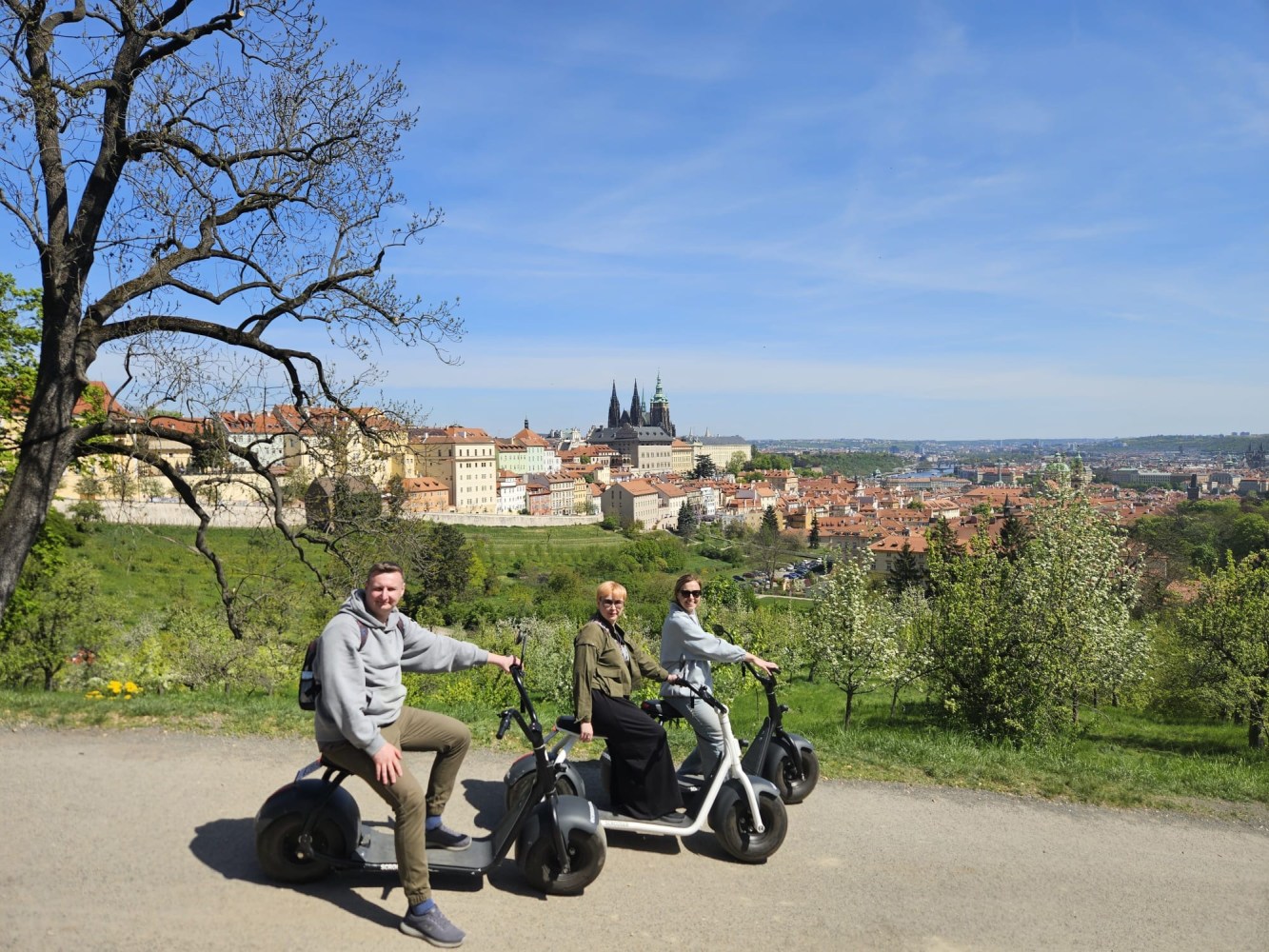 Three people on scooters with cityscape and greenery in the background.