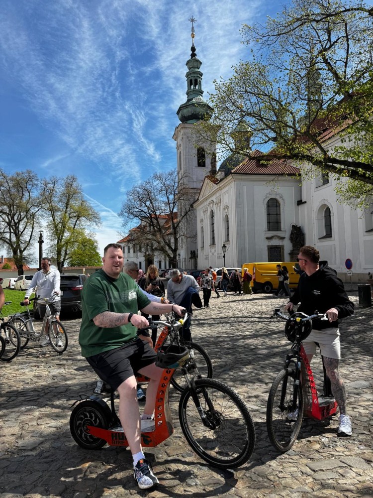 Cyclists on a cobblestone street near a historic building and church on a sunny day.