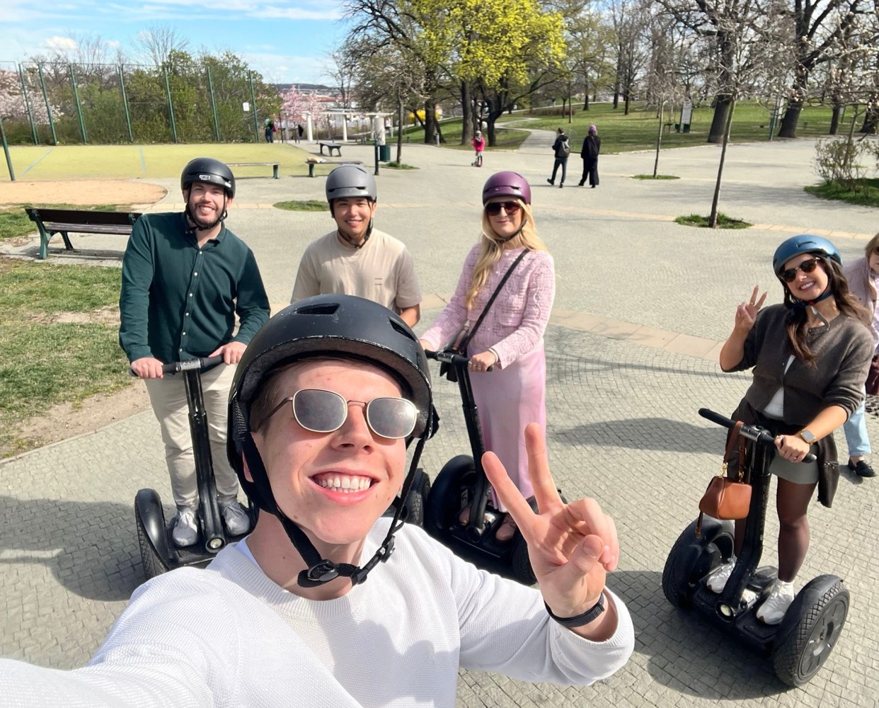 Five people wearing helmets, smiling on Segways in a park setting.