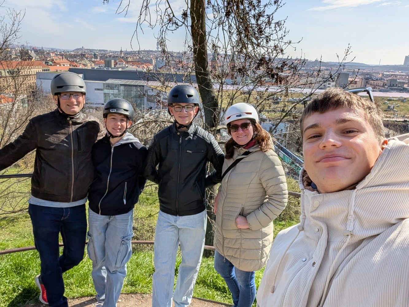 Five people in helmets posing with a cityscape in the background on a sunny day.