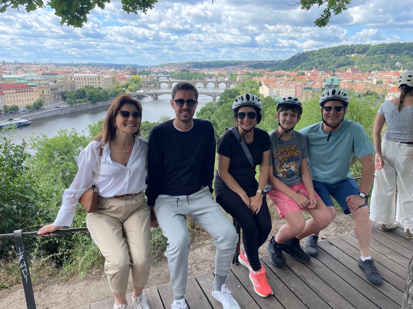 Group of five people with helmets posing on a scenic overlook with river and bridges in the background.
