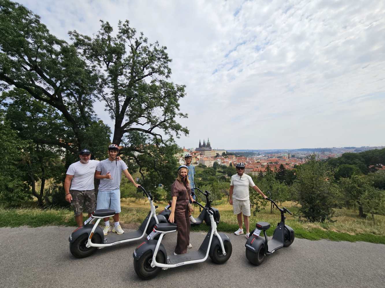 Four people on scooters with helmets, overlooking cityscape with distant cathedral.