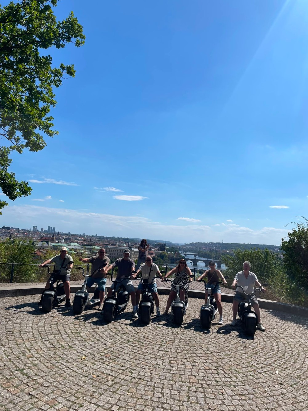 Group of people on scooters on a sunny day with cityscape background.