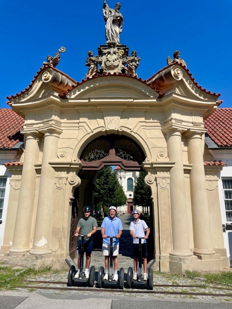 Three people on segways in front of an ornate archway under a clear blue sky.